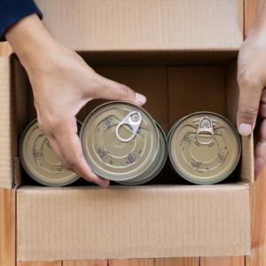 Hands packing canned food into a box