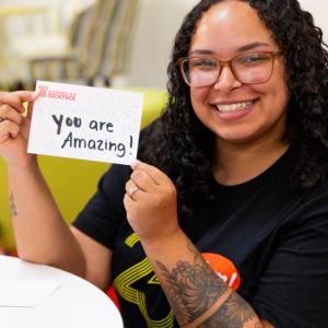 Volunteer holding sign reading "you are amazing!"