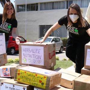 Two volunteers stand outside behind many stacked and hand decorated boxes