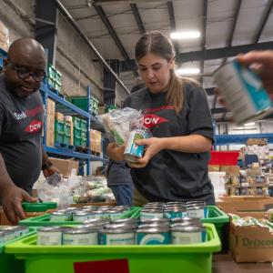 Volunteers sorting cans of food in a warehouse setting.