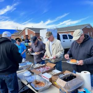 People in line assembling food plates in a parking lot.