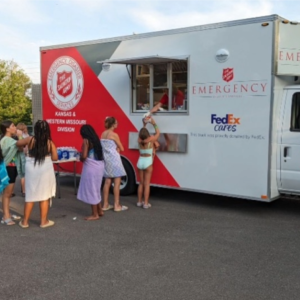 A line of people in front of a truck with side window opening.