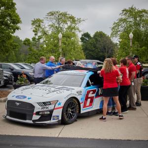 a group of people stand outside and take a cover off a race car. "6" on the side