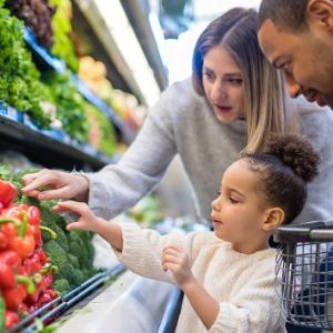 Two adults and a child looking at fresh vegetables in a grocery store.