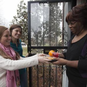 two people deliver a packaged meal to a person in a home
