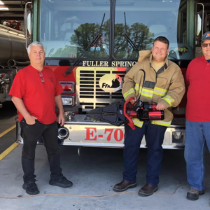 three people standing in front of a fire truck. One holding a 'jaws of life'.