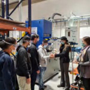 A group of people in protective masks in an industrial setting. Two hold hands.