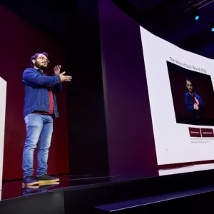 Gabriel presenting on stage using sign language and a digital display.