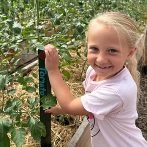 A smiling child holding on to a post in a raised garden with walkways.