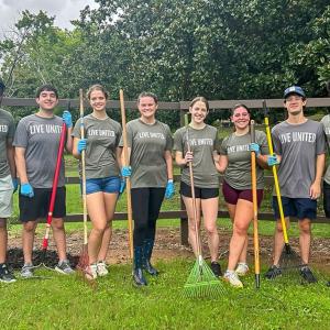 A group of volunteers posed in front of a fence with garden tools.