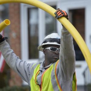 A utility worker holding up a yellow tube outside.