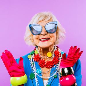 Older, smiling woman wearing big sunglasses and rainbow pride colors for accessories.