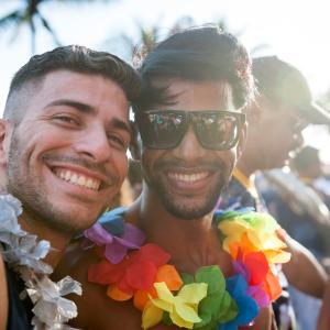 Two people wearing lai's in rainbow colors. Both are smiling.