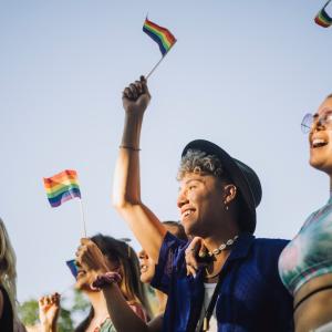 A group of individuals that are smiling and holding small rainbow flags.