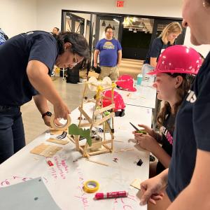 Adult volunteers and children working on building model structures with craft supplies.
