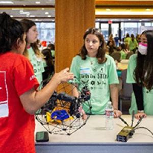 students working on a robotics project in a large room with others