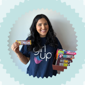 A smiling person wearing a "Girl up" t-shirt, holding up a Hershey bar.