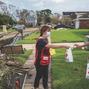 an american red cross volunteer handing a bag to another person, debris on the ground