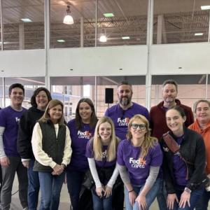 A group of people in FedEx Cares t-shirts posing inside a building