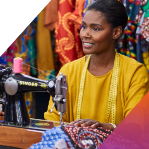 A person sitting behind a sewing machine. Bright colored fabrics behind them.