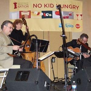 A small band playing on a stage. "No Kid Hungry" banner behind them.