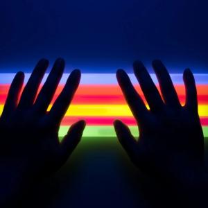 two hands back-lit by a rainbow of colors