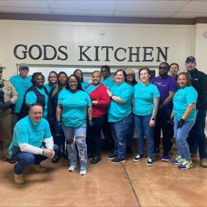 A group of volunteers posed in front of an indoor sign  "Gods Kitchen".