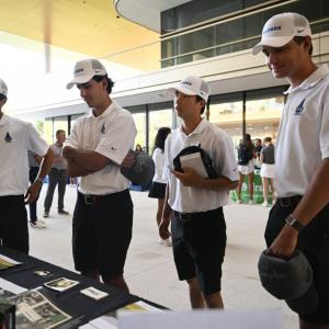 Four standing people in matching clothes look at a booth with materials on it.