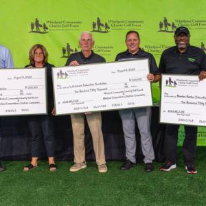 Representatives from local schools pose with large checks