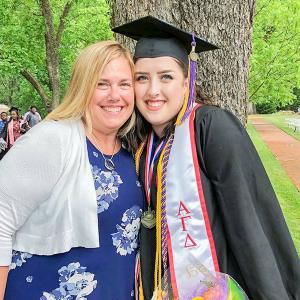 Danielle in a graduation cap and gown outside, hugging another