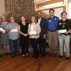 A group posed in front of a fireplace, many holding checks.
