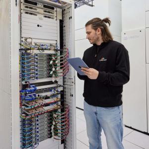A person with an electronic device looking at a tall box with many wires and computer parts.