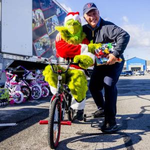 A person dressed as the Grinch on a bicycle, hugging a volunteer.