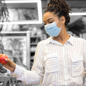 a person holds a red apple in a grocery store, a basket in their other hand