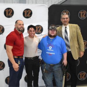 Four people stood next to each other smiling with a 12 for Life®  backdrop behind them