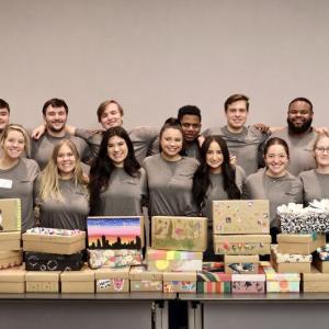 large group of people behind a table of stacked shoeboxes