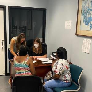 People seated on both sides of a desk talking, another standing by.