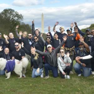 A group of people posed outside, smiling with raised hands. The Washington Monument in the distance.