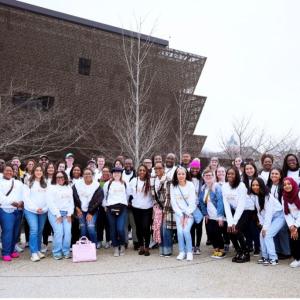 Over 50 Bath & Body Works associates are smiling pictured together in matching shirts in front of the National Museum of African American History and Culture. The museum building is in the background.