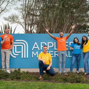 group smiling in front of Applied Materials logo