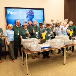 Group of volunteers posed, giving thumbs-up, behind a table of bins.