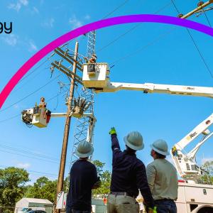 Four people in hard hats looking up at two in lift trucks working on power lines.