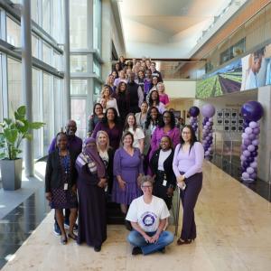 A group of people posed next to purple balloons and big windows