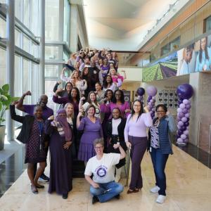 A group of people posed next to purple balloons and big windows
