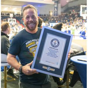 A person holding an official, framed, certificate from Guinness world records. A crowded stadium and basketball court behind them.