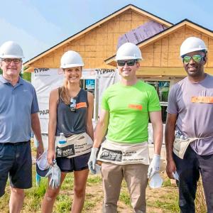 Four people posed outside a home being built