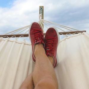 two feet with red shoes propped up in a hammock, a partly cloudy sky behind