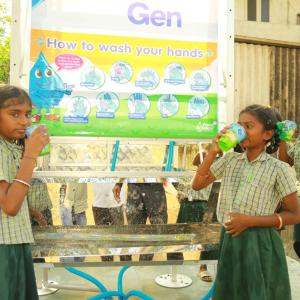 Three children drinking from cups at a water station.