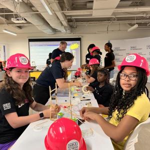 Adult volunteers and children working on building model structures with craft supplies.