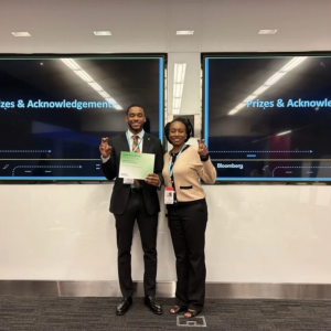 Two participants standing in front of digital displays, holding a certificate.